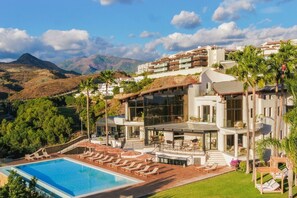 A modern resort with a swimming pool, lounge chairs, and a view of the mountains.