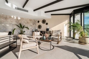 Un salon moderne avec un mur en pierre, de grandes fenêtres et un mélange de meubles, notamment des canapés et des fauteuils.