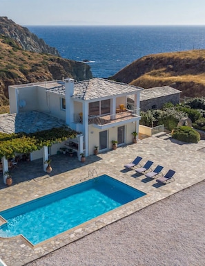 Una casa moderna de dos pisos con piscina, mobiliario exterior y vista al océano.