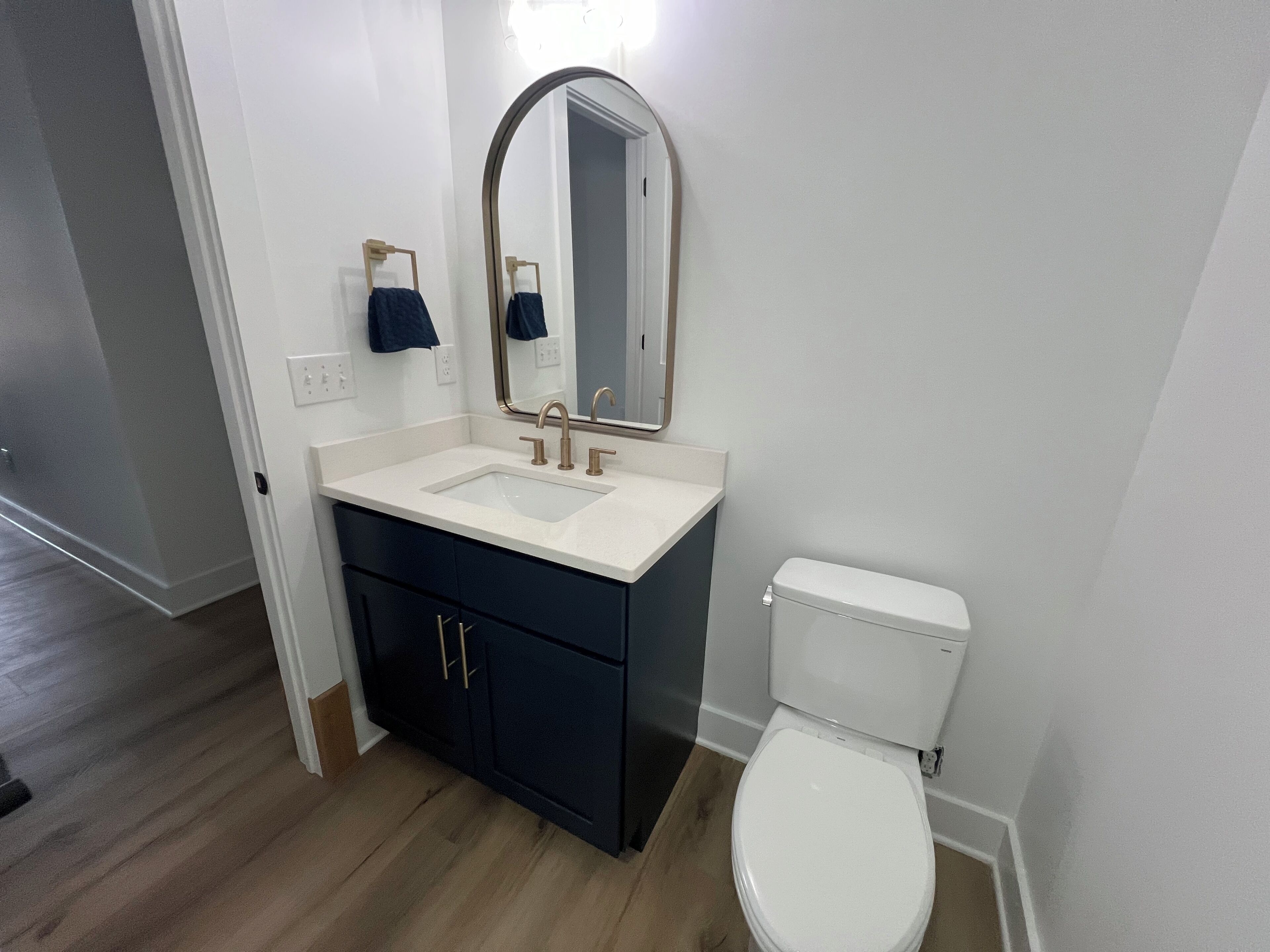 A bathroom with a white sink, dark cabinets, a white toilet, and a mirror.