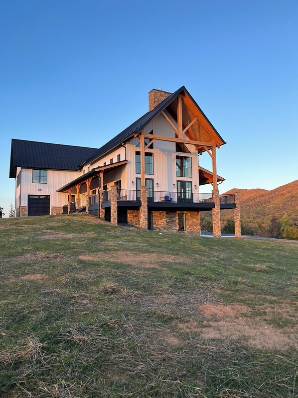 A large, two-story house with a prominent stone chimney, multiple balconies, and a spacious front porch.