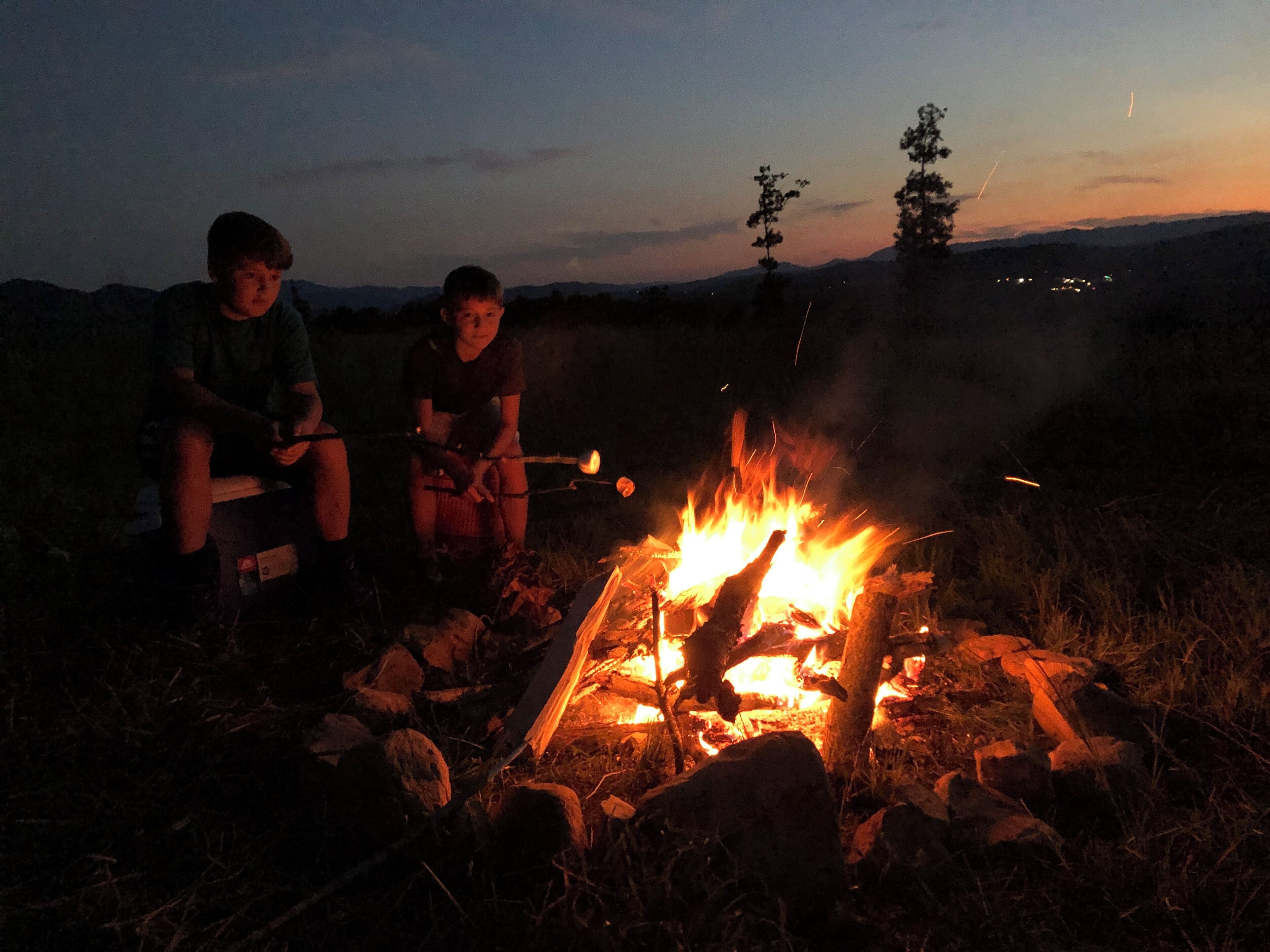 Deux personnes assises près d’un feu de camp, dans un cadre naturel.