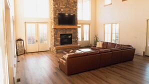 A spacious living room with a stone fireplace, a large leather sofa, and a flat-screen TV mounted on the wall. - Meridian House - A Blue Ridge Mountain Escape for Memories (Buena Vista)