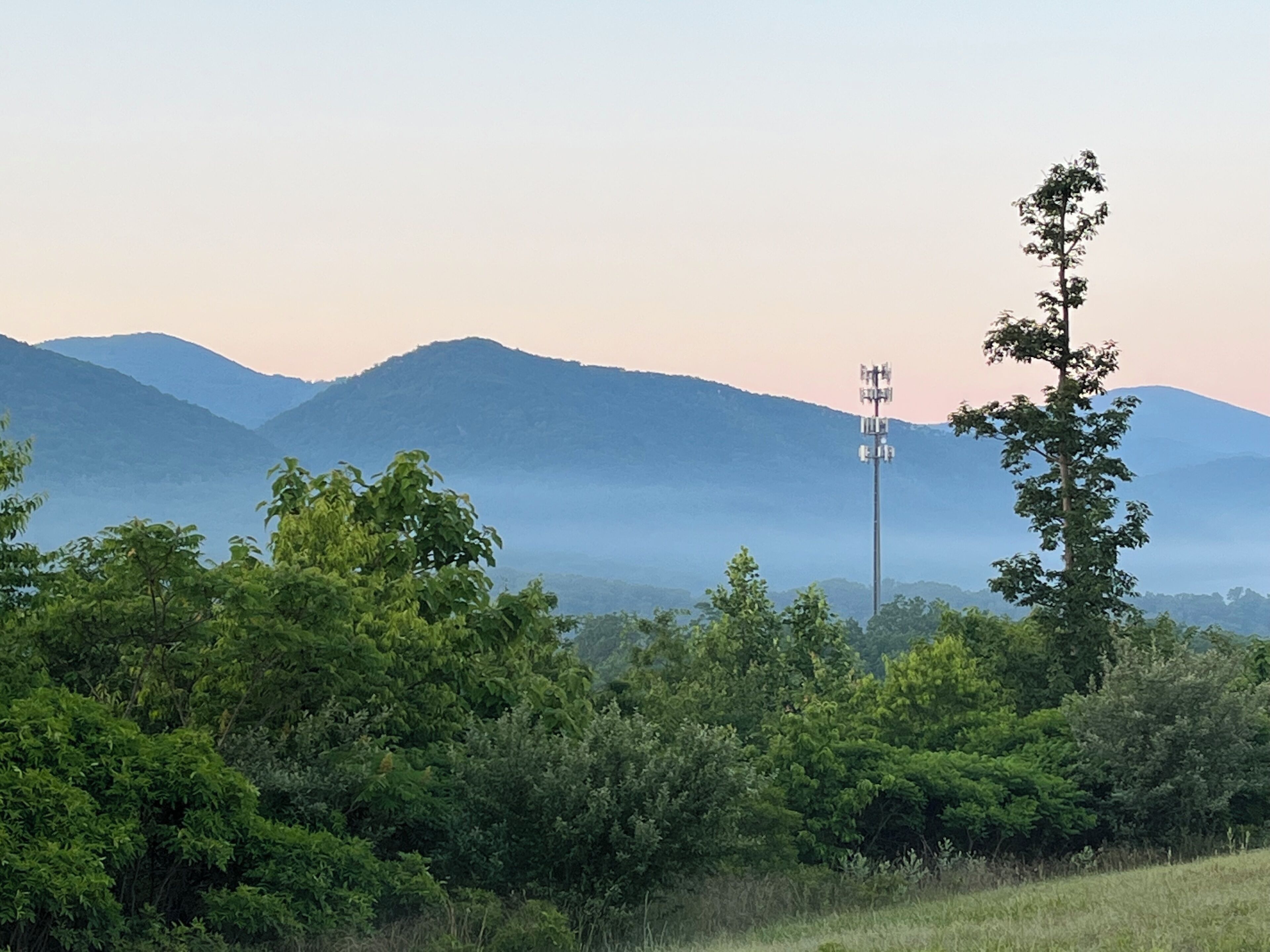 A landscape with a clear sky, a mountain range, and a communication tower.
