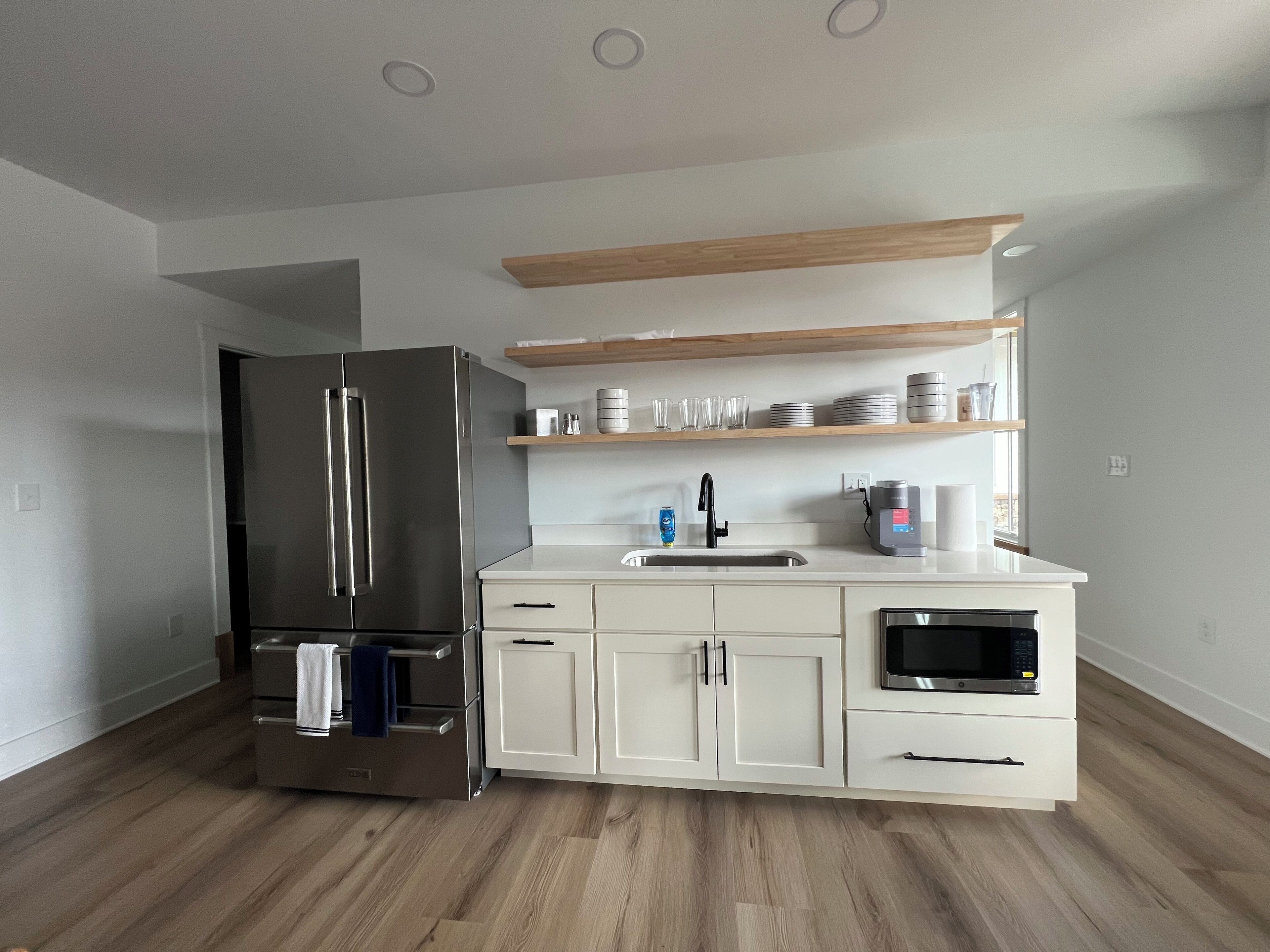 A modern kitchen with white cabinetry, a stainless steel refrigerator, a microwave, and a coffee maker.