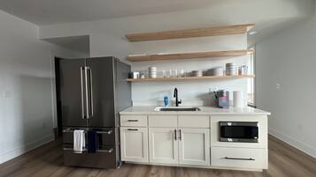 A modern kitchen with white cabinetry, a stainless steel refrigerator, a microwave, and a coffee maker.