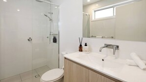 Une salle de bain moderne avec une douche à parois de verre, des toilettes blanches, un lavabo avec un miroir et une fenêtre située au-dessus du miroir.