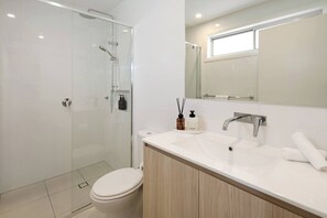A modern bathroom with a glass-enclosed shower, a white toilet, a sink with a mirror, and a window above the mirror.