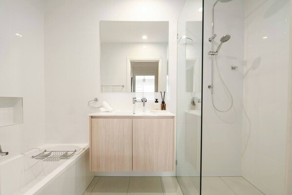 A modern bathroom with a glass-enclosed shower, a wooden vanity, and a bathtub.