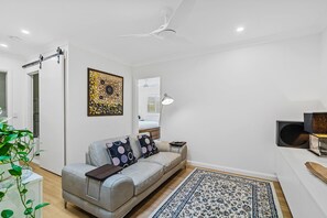 A modern living room with a grey sofa, a patterned rug, and a ceiling fan.