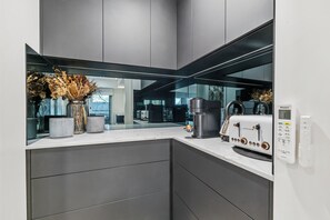 Una cocina moderna con horno empotrado, cafetera y un jarrón decorativo con flores secas.