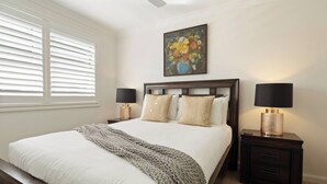 Une chambre à coucher avec un grand lit, deux tables de chevet avec des lampes, un tableau au-dessus du lit et une fenêtre avec des stores.