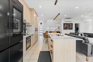 Eine moderne Küche mit Backofen, Kühlschrank und Essbereich inklusive Sofa und Couchtisch.
