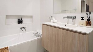 Une salle de bain moderne avec une baignoire, un lavabo et un miroir. Il y a deux bouteilles sur l'étagère au-dessus du lavabo et une serviette sur le comptoir.
