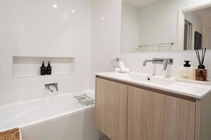 A modern bathroom with a bathtub, a sink, and a mirror. There are two bottles on the shelf above the sink and a towel on the counter.