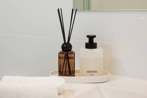 A bathroom with a white sink, a white towel, a brown reed diffuser, and a white hand soap dispenser.