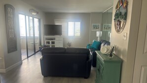 Un salón amplio con un sofá seccional negro grande, un mueble verde y un televisor de pantalla plana.