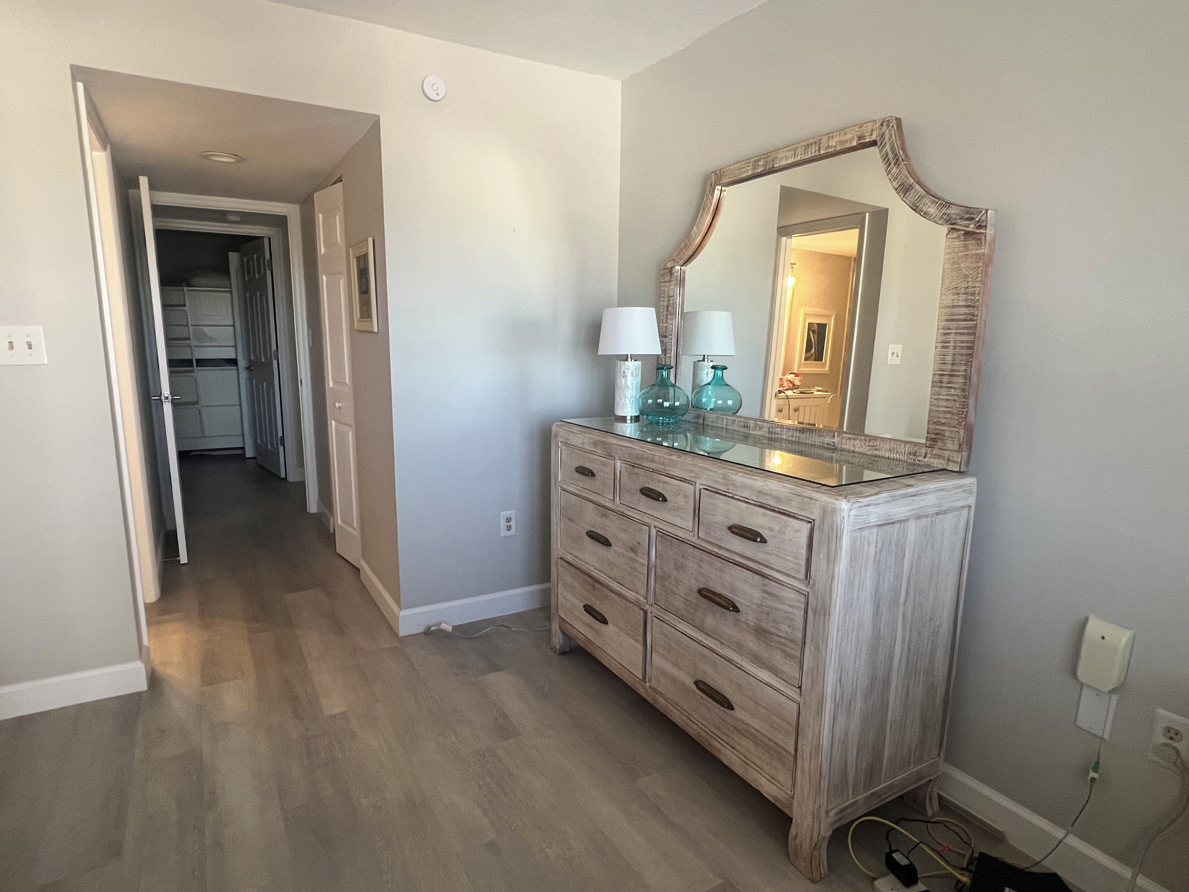 A hallway with a wooden dresser, a mirror, and a door leading to another room.