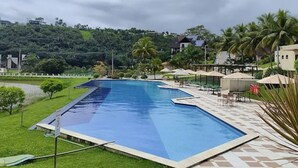 Una piscina con borde de baldosas, rodeada de césped y palmeras, con vistas a un paisaje montañoso al fondo.