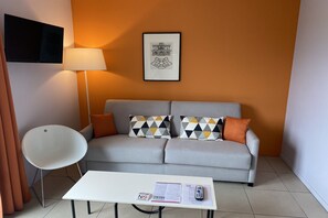 Una sala de estar moderna con un sofá gris, cojines estampados, una mesa de centro blanca con documentos, una silla blanca y una lámpara de pie.