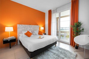 A modern hotel room with a large bed, two bedside lamps, a white chair, and a view through a glass door.