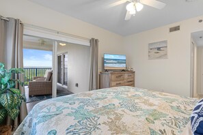 Ein Schlafzimmer mit Bett, Fernseher, Kommode, Topfpflanze und einem Balkon mit Stuhl.