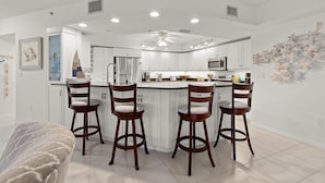 Una cocina moderna con armarios blancos, una isla central con taburetes de bar y un ventilador de techo.