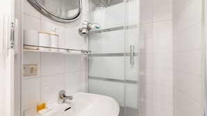 Ein modernes Badezimmer mit einem weißen Waschbecken, einer Duschkabine aus Glas und einem Spiegel über dem Waschbecken.
