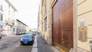 Eine enge Straße mit parkenden Autos, ein blauer Wagen im Vordergrund und eine große Holztür auf der rechten Seite.