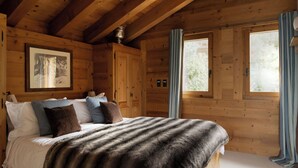 Un dormitorio de cabaña de madera con cama, almohadas, un plaid de piel, una foto enmarco y una ventana con cortinas.
