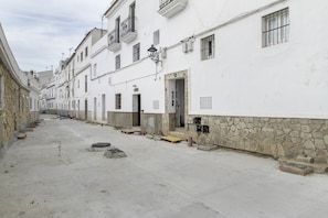 A narrow street lined with white buildings, some with stone bases, and a few balconies.