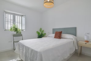 A bedroom with a bed, bedside table, lamp, and two potted plants.