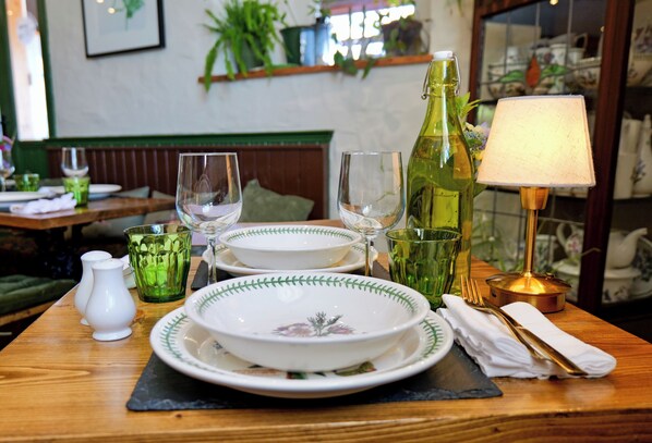 Une table à manger dressée avec des assiettes, des verres, une bouteille, une lampe et une serviette.