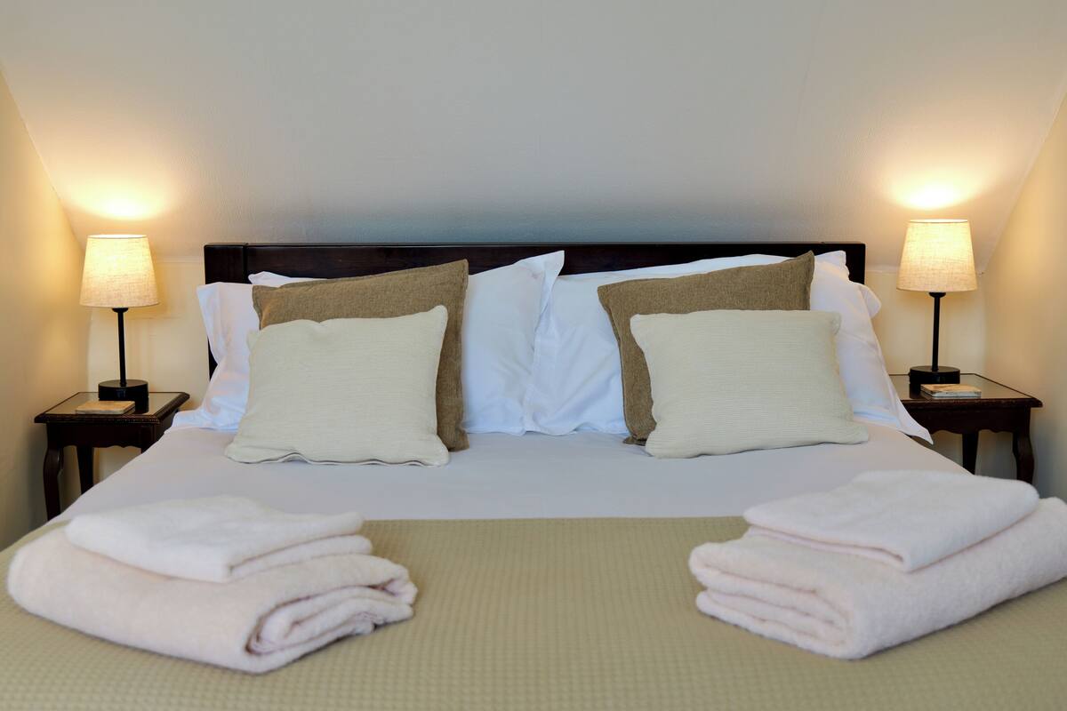 A neatly made bed with pillows, two bedside lamps, and folded towels on a textured bedspread.