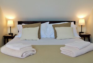 Una cama bien hecha con almohadas, dos lámparas de noche y toallas dobladas sobre un edredón con textura.
