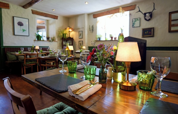 Un comedor con mesas de madera, vasos de vidrio verde y una lámpara.