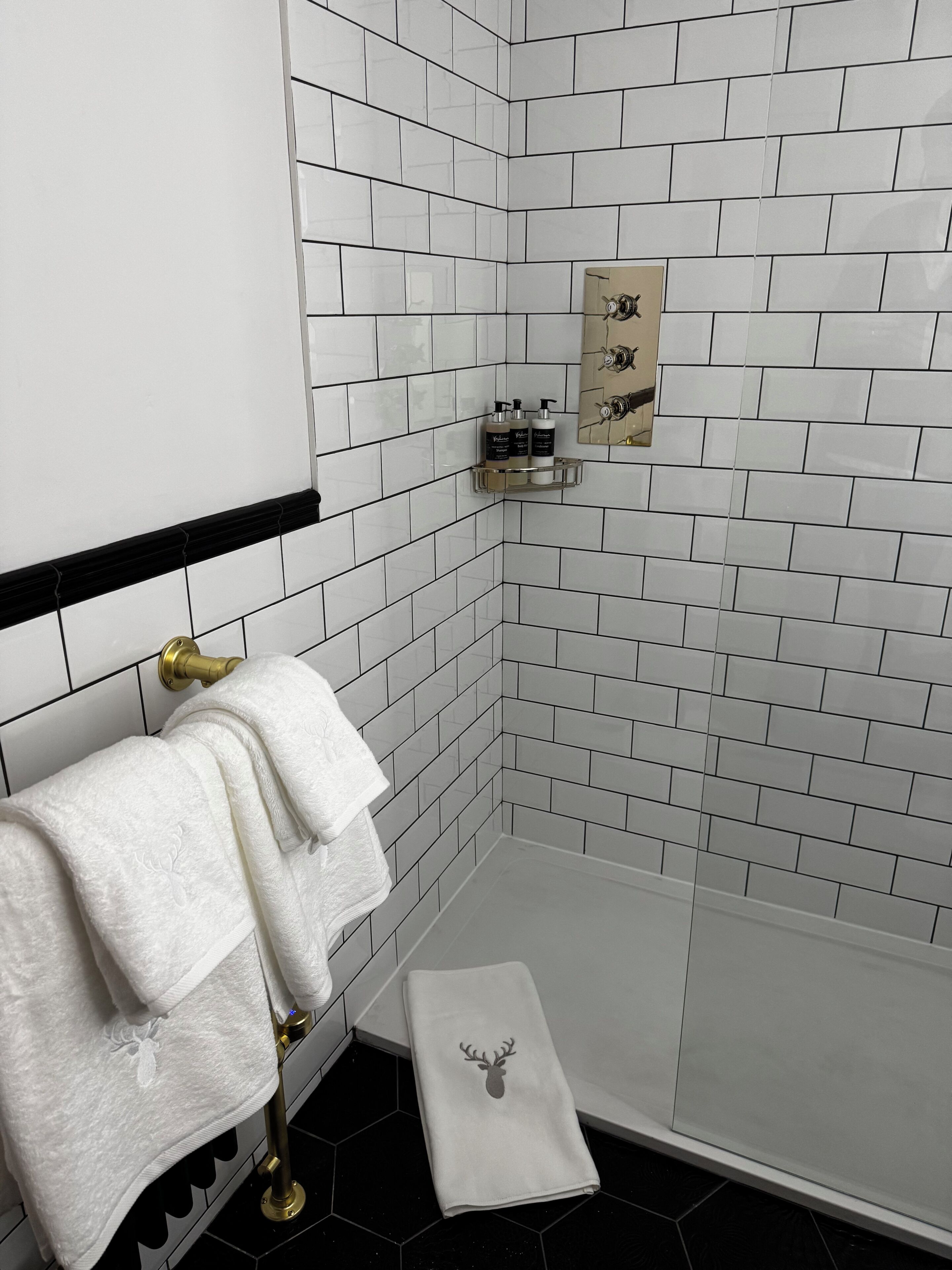 A bathroom with white tiled walls, a shower area, and a towel rack with two towels.