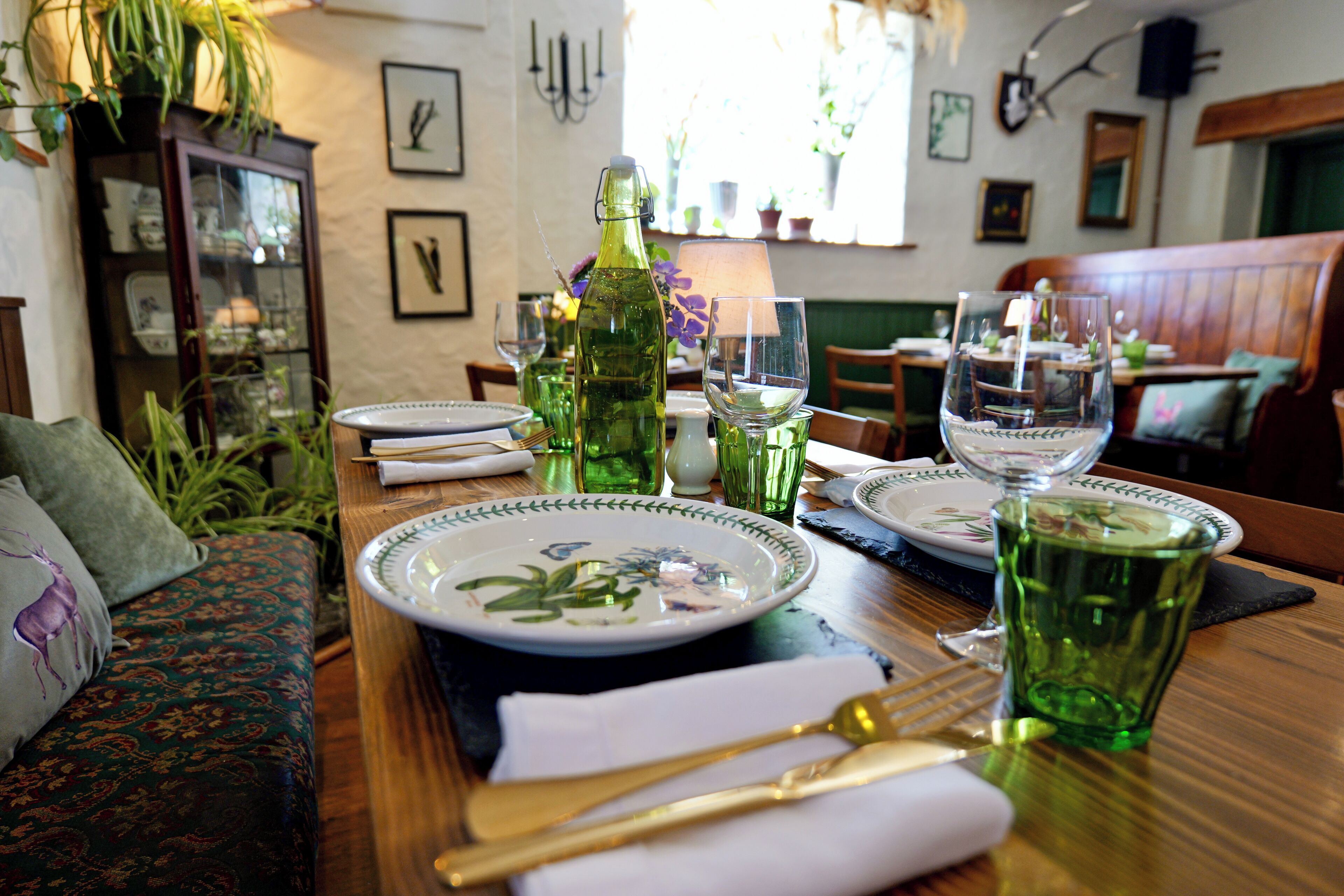 A dining table set with plates, glasses, and cutlery, surrounded by a sofa and a cabinet with glass doors.