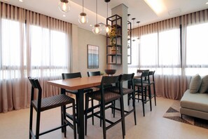 A modern dining area with a wooden table and black chairs, surrounded by large windows with sheer curtains. - Boulevard Agami (São Paulo)