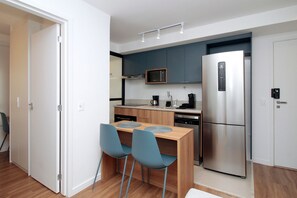 A compact kitchen with a microwave, refrigerator, coffee maker, and a dining area with two chairs. - Boulevard Agami (São Paulo)