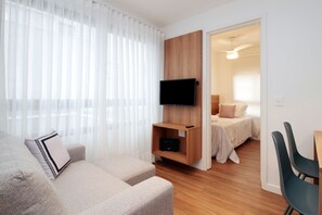 A modern living room with a sofa, a mounted TV, and a wooden shelf. - Boulevard Agami (São Paulo)