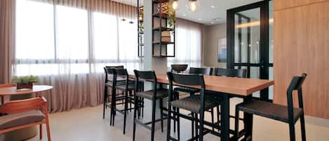 Un comedor moderno con una mesa de madera y sillas negras, una pequeña mesa redonda con una planta y una estantería con objetos decorativos.