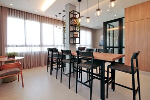 A modern dining area with a wooden table and black chairs, a small round table with a plant, and a bookshelf with decorative items. - Boulevard Agami (São Paulo)