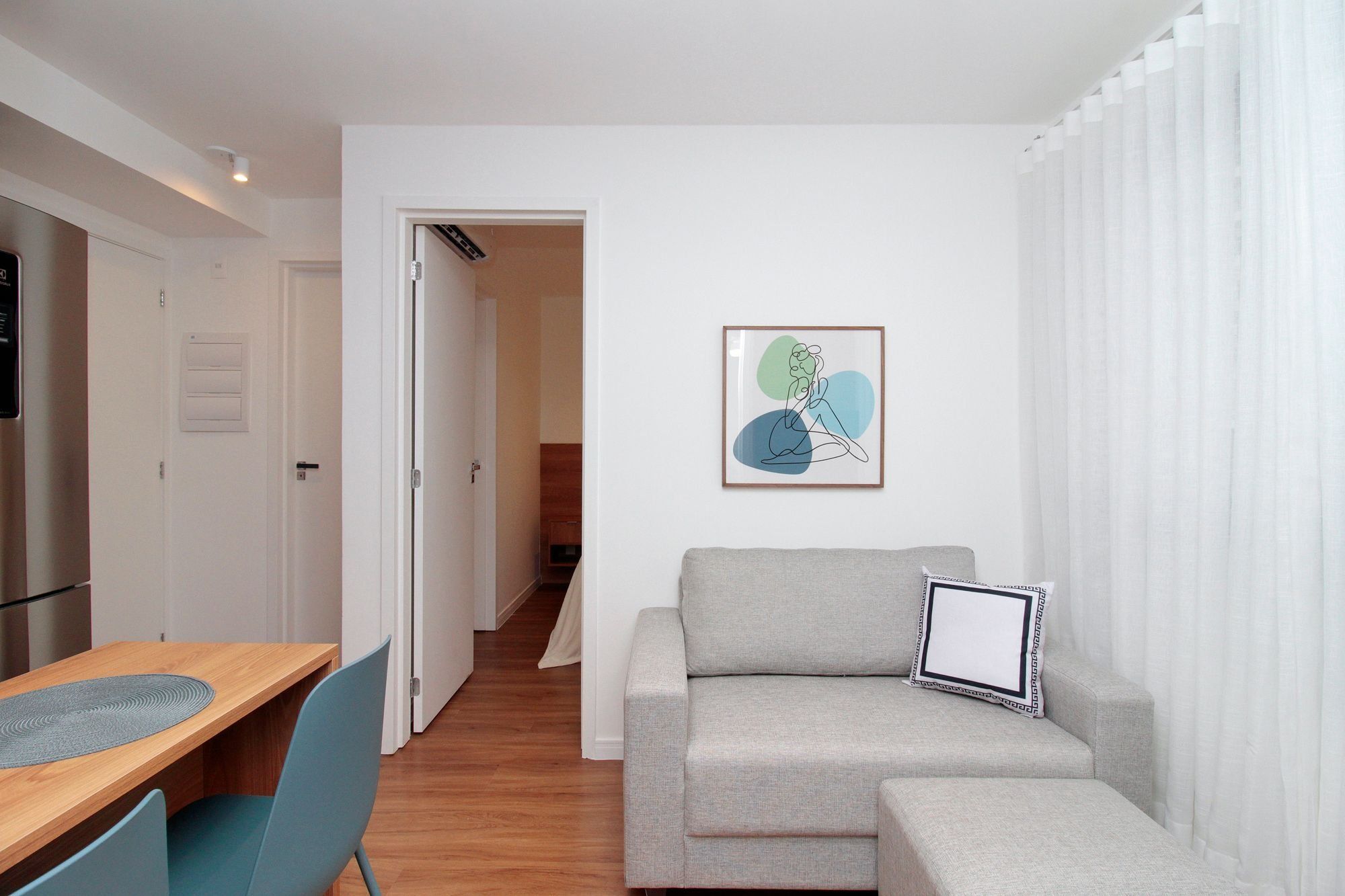 A modern living room with a sofa, a dining table with chairs, and a hallway leading to another room.