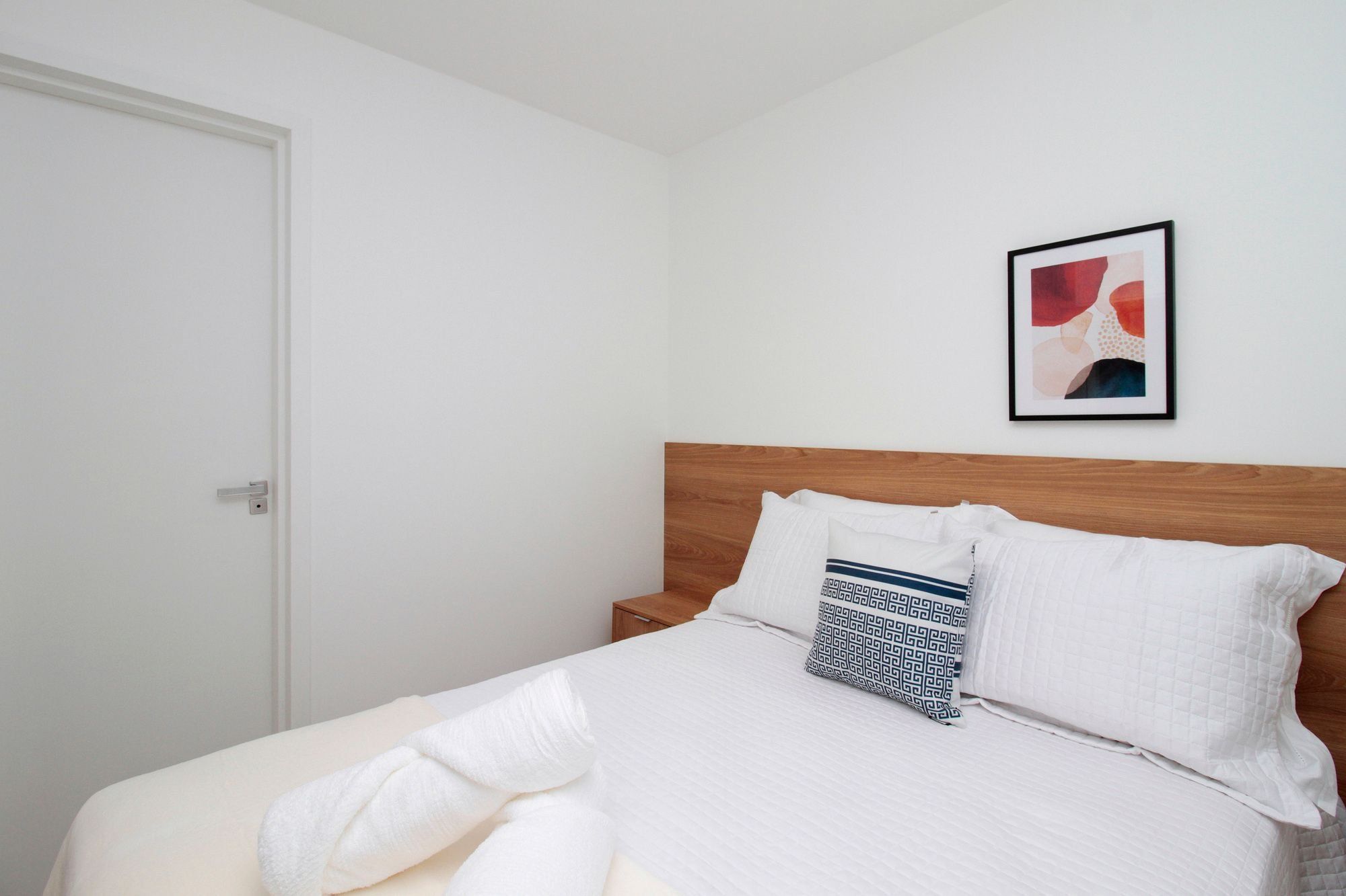 A neatly made bed with a wooden headboard, white bedding, and a patterned pillow.