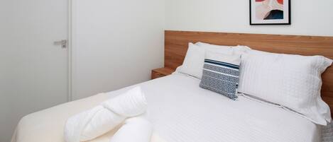 A neatly made bed with a wooden headboard, white bedding, and a patterned pillow.