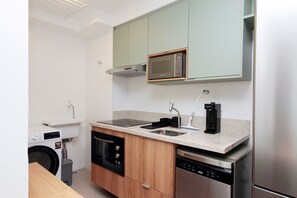 A compact kitchen with a microwave, stove, sink, dishwasher, and a washing machine. - Boulevard Agami (São Paulo)