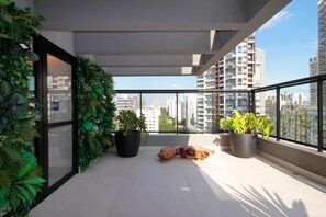 A balcony with potted plants, a wooden sculpture, and a city view. - Boulevard Agami (São Paulo)