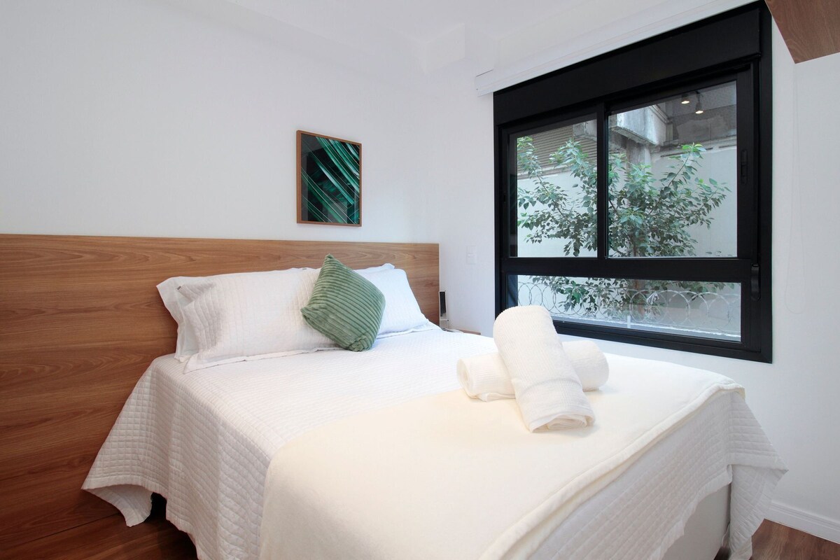 A neatly made bed with a wooden headboard, a green pillow, and a rolled towel on the bed.