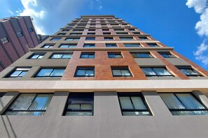 A high-rise building with a modern architectural design, featuring a mix of brick and concrete facades, multiple windows, and a clear sky in the background. - Boulevard Agami (São Paulo)